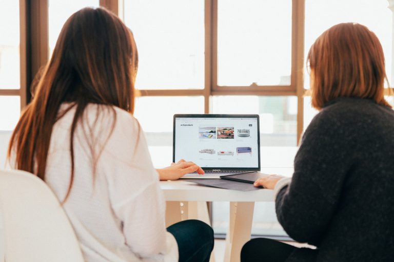 Two women in front of a laptop talking about features of a successful real estate website.